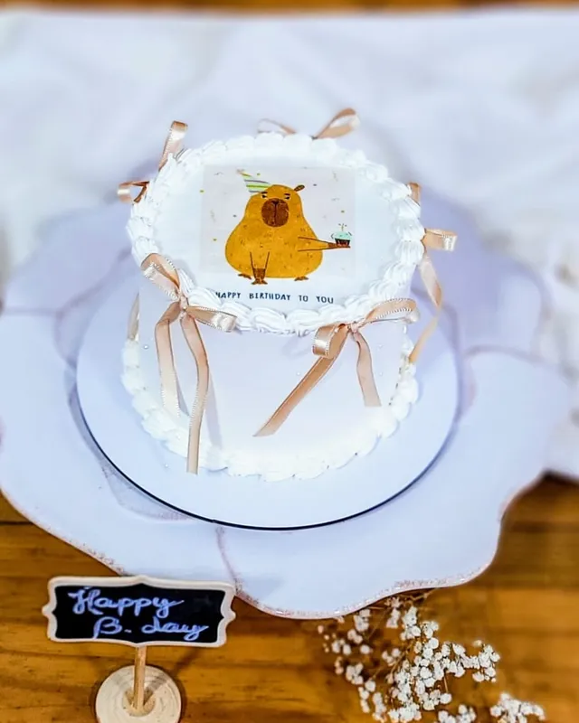 Bolo branco com desenho de capivara e laços bege de cetim