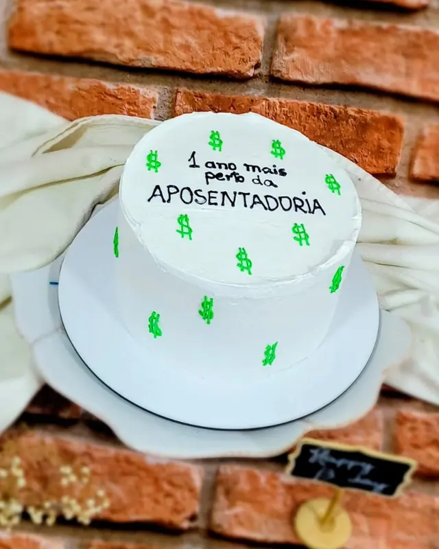 Bolo branco com confeitos verdes e o tema aposentadoria escrito à mão